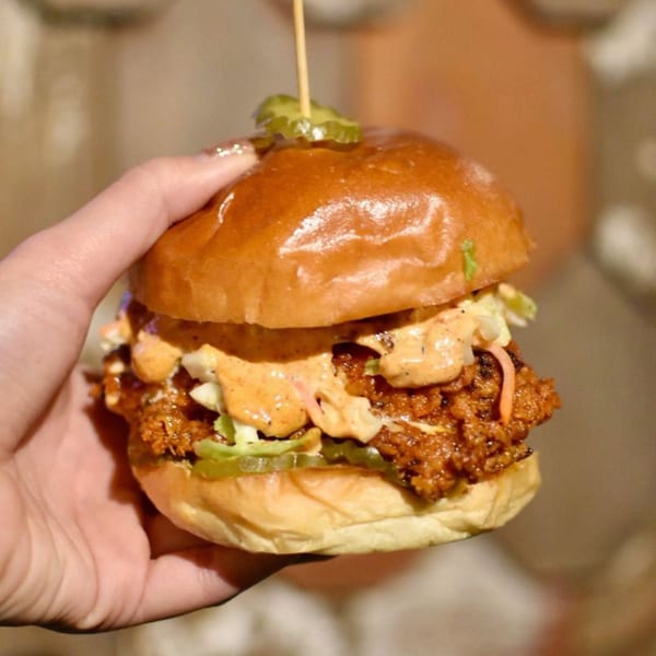 Hand holding a Double Chin Asian-fusion fried chicken sandwich with sauce, slaw, and pickles.