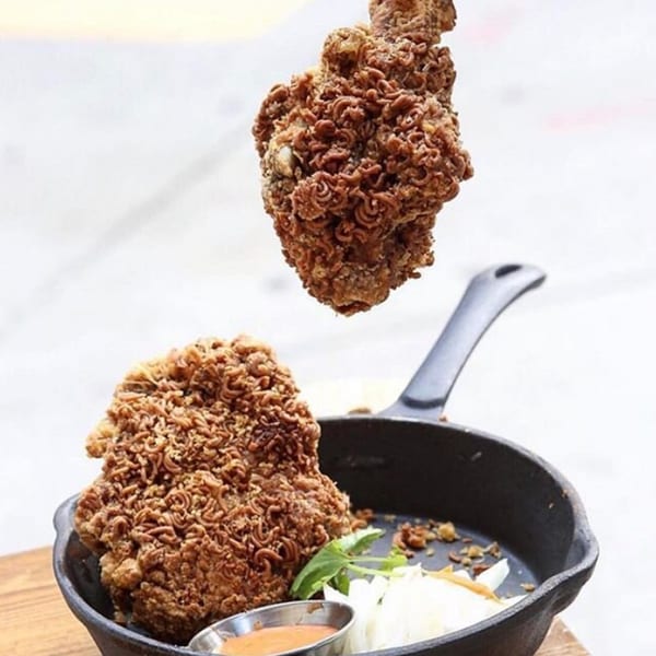 Double Chin's crispy ramen-crusted fried chicken, with one piece levitating above a cast iron skillet.